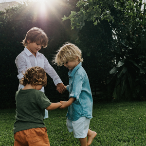 Three boys holding hands in a circle outside on the grass
